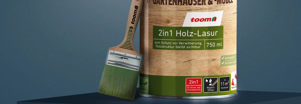 Ein Gebinde toom 2in1 Holzlasur steht mit einem Pinsel auf einem Sockel